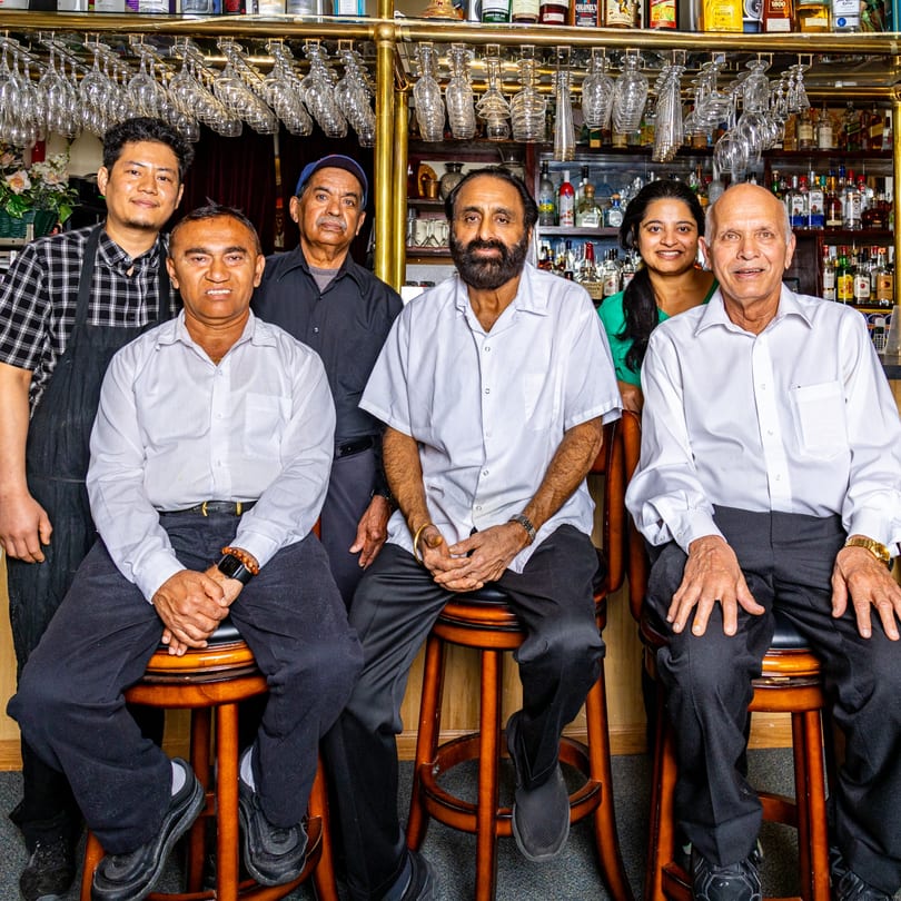 Six INDIA'S Restaurant staff members, including men and one woman, pose in front of a bar.