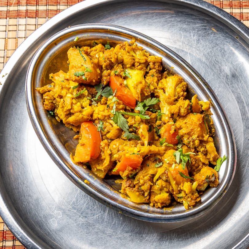 Aloo Gobi, an Indian dish with cauliflower, potatoes, and tomatoes, garnished with cilantro in a metal bowl.