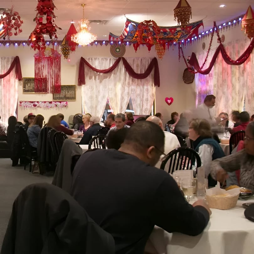 Diners seated at tables in INDIA'S Restaurant, adorned with festive red and gold Indian decorations.