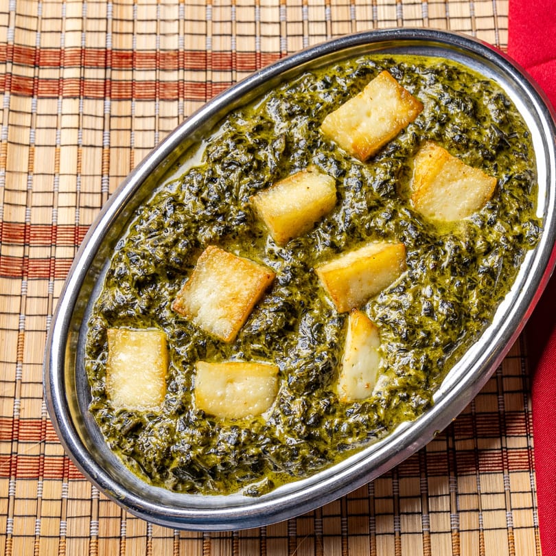 Palak Paneer, a vibrant green Indian spinach and cheese dish, in a silver oval bowl.