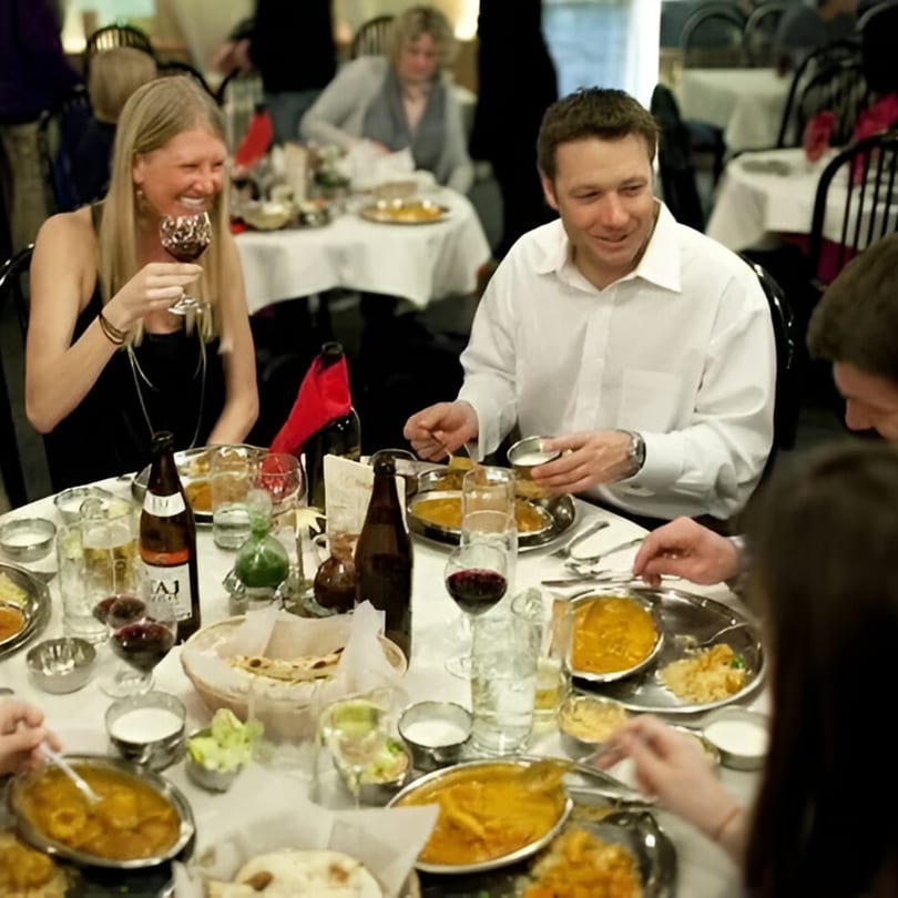 Happy diners enjoying Indian food and drinks at a table in INDIA'S Restaurant.