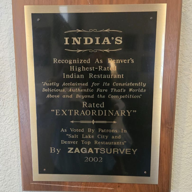 A wooden plaque with a black and gold plate recognizing INDIA'S as Denver's highest-rated Indian restaurant.