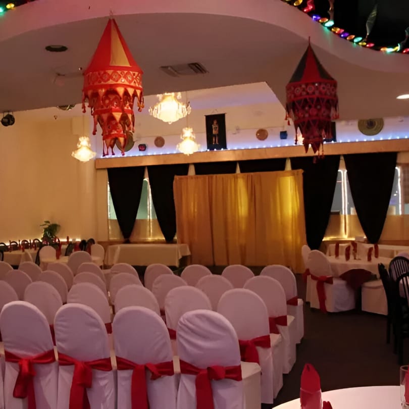 An event space at INDIA'S Restaurant with rows of white chairs with red sashes and decorated ceilings.
