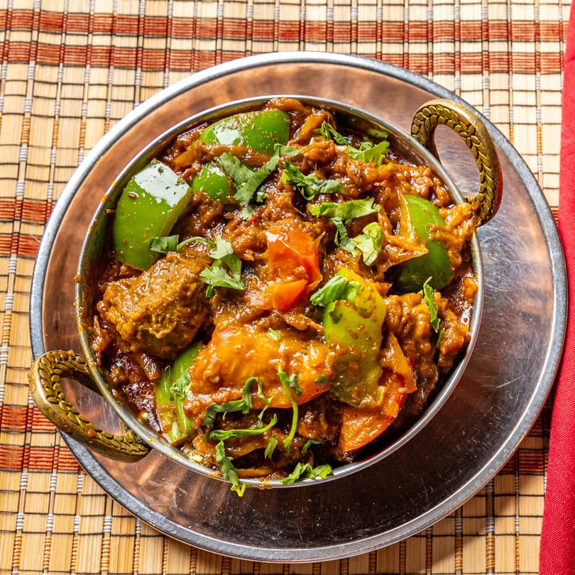 Close-up of Indian curry with meat, green bell peppers, and cilantro in a metal bowl.