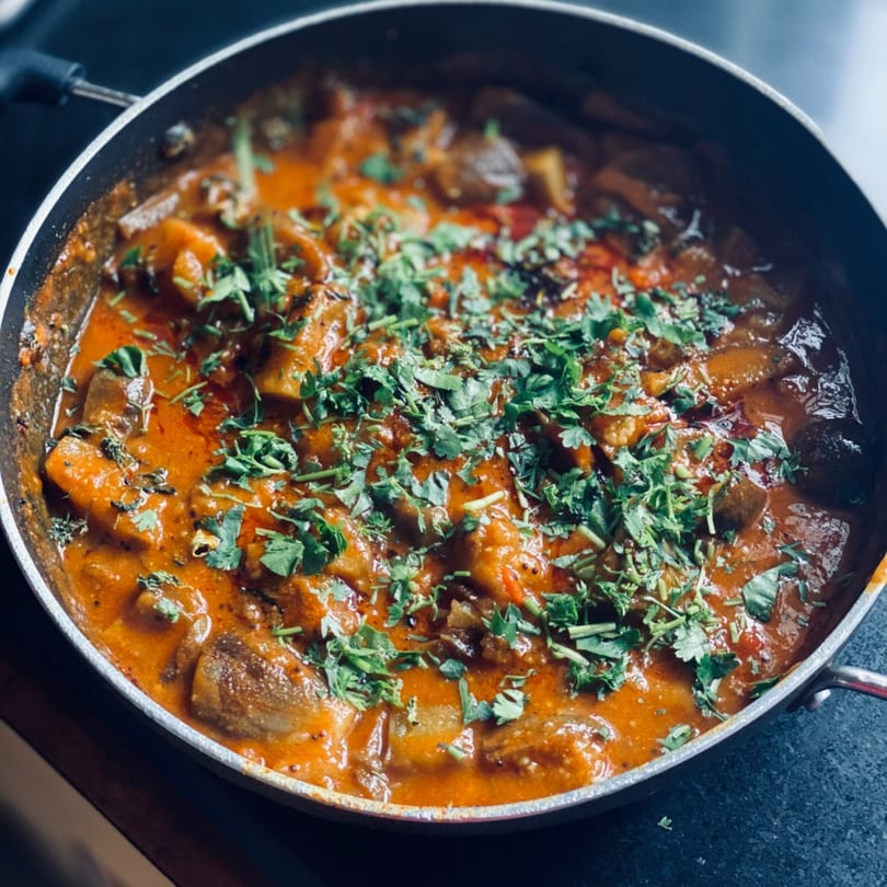 Close-up of a pan filled with a rich, orange curry dish, garnished with fresh green cilantro.