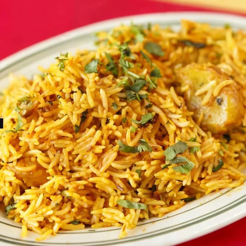 A close-up of a plate of golden biryani rice with cilantro garnish and potatoes.