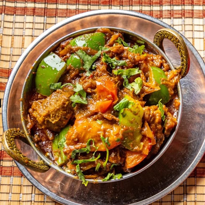 Close-up of a karahi dish with meat, green peppers, and cilantro in a metal bowl.