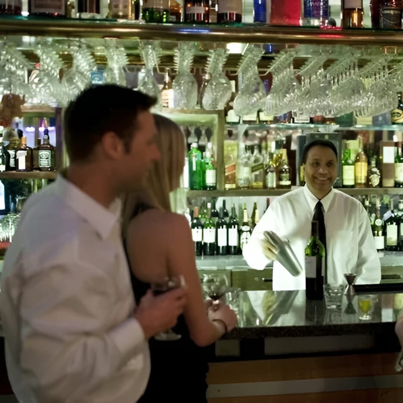Bartender smiling behind a bar with a couple enjoying drinks at INDIA'S Restaurant.